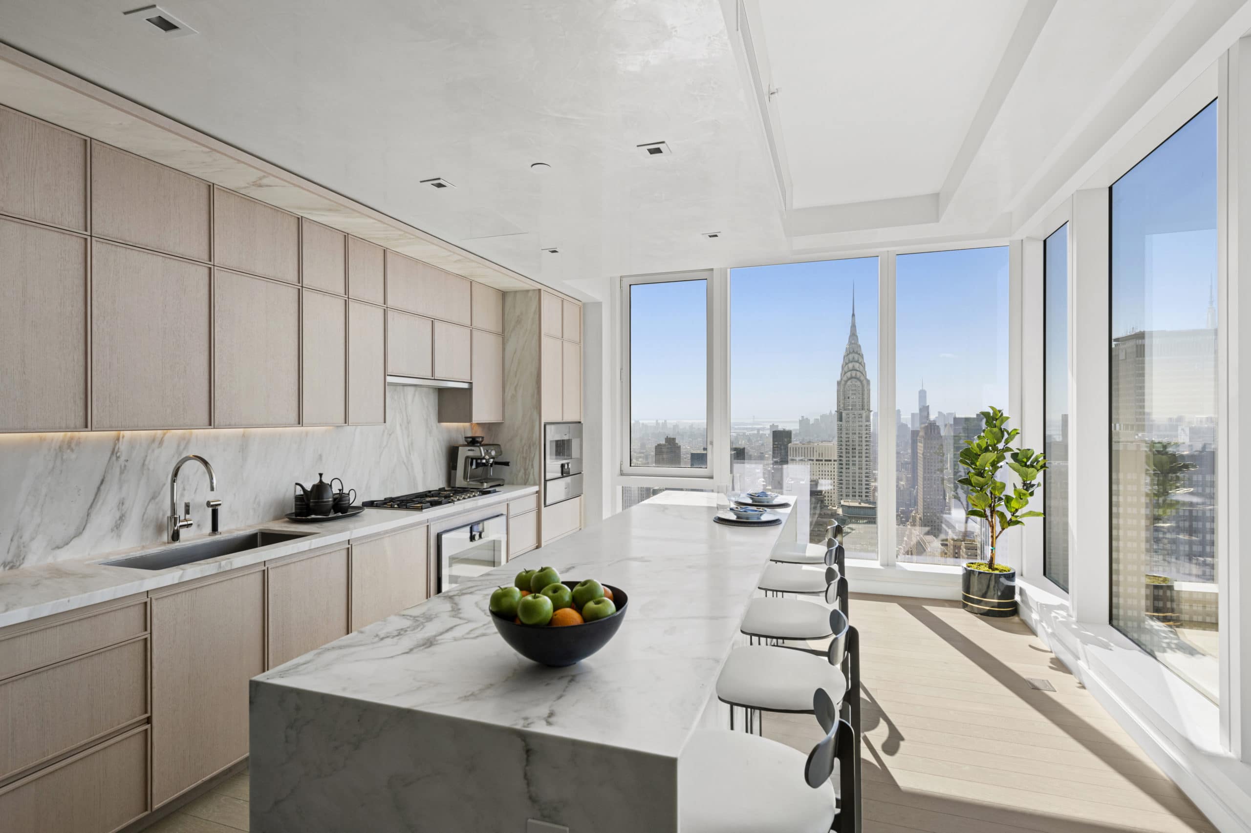 Kitchen in The Centrale condos in NYC. Tan cabinets, white marble countertops, a long island and chairs with city views.
