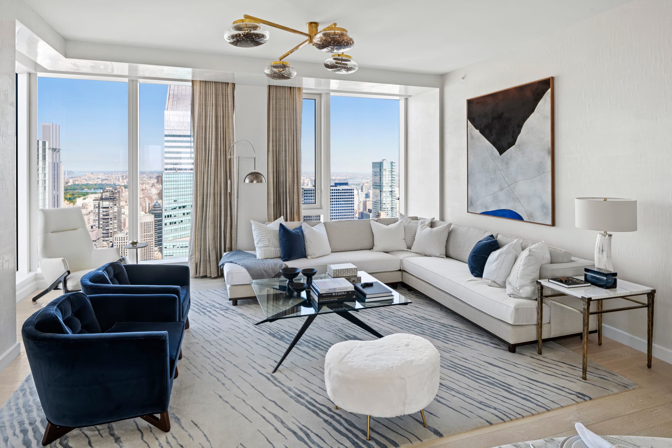 Corner living room with floor-to-ceiling windows, blue chairs, and a white couch overlooking New York at The Centrale condos.