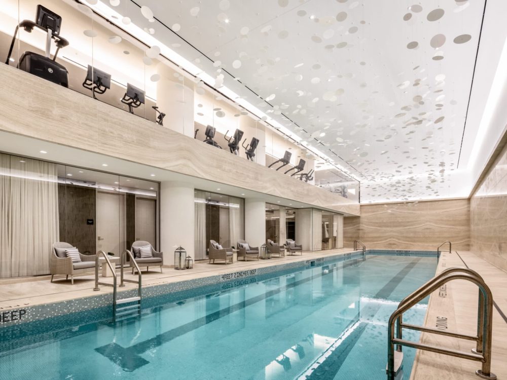 Pool at The Centrale luxury condos in NYC. Pool room with High ceilings, hanging art and chairs with a workout room above.