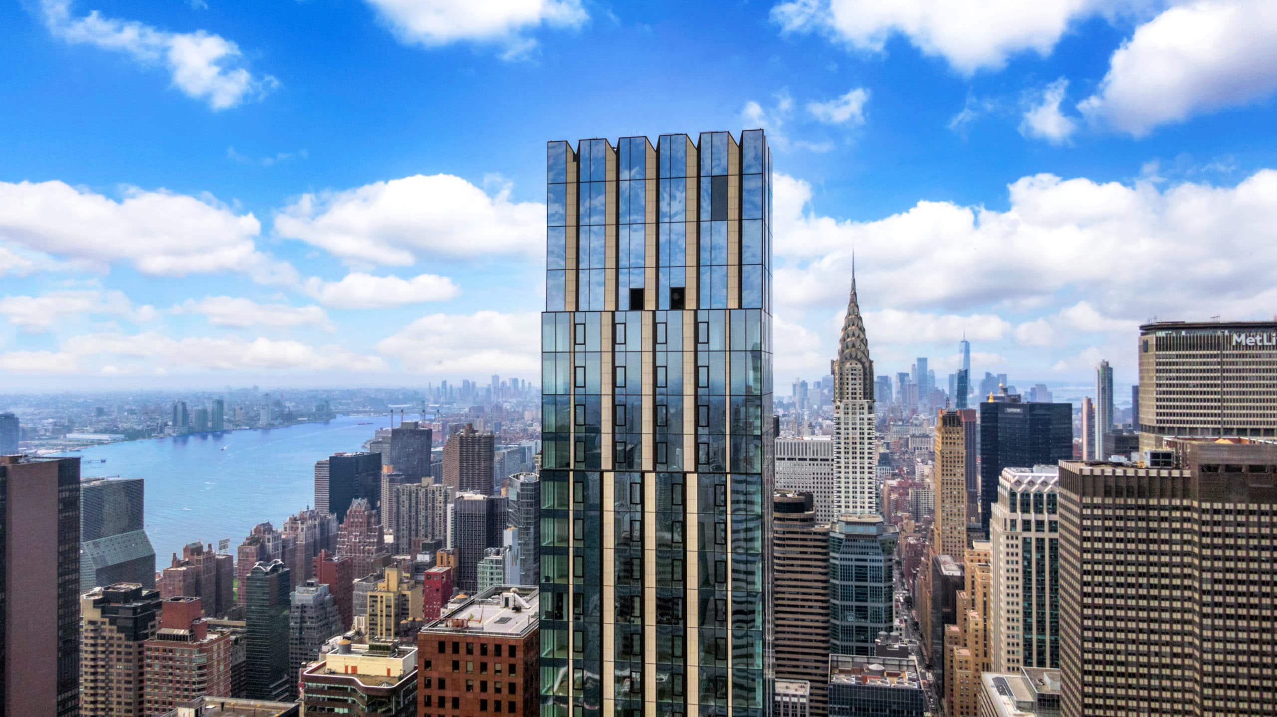 Birds eye view of The Centrale luxury condominiums in New York with city skyline in the background with blue skies.