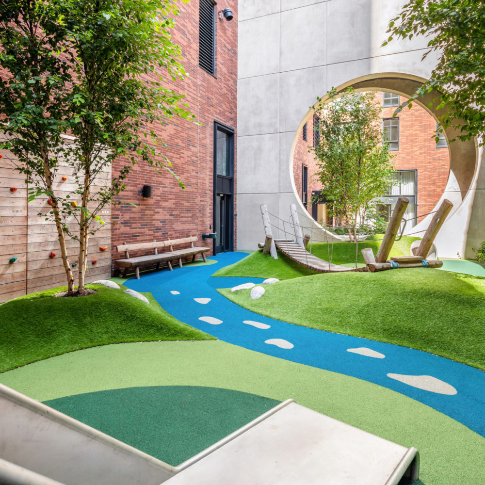 Kids playroom at The Kent condominiums in New York. Outdoor park theme with slide, turf floor, trees and a climbing wall.