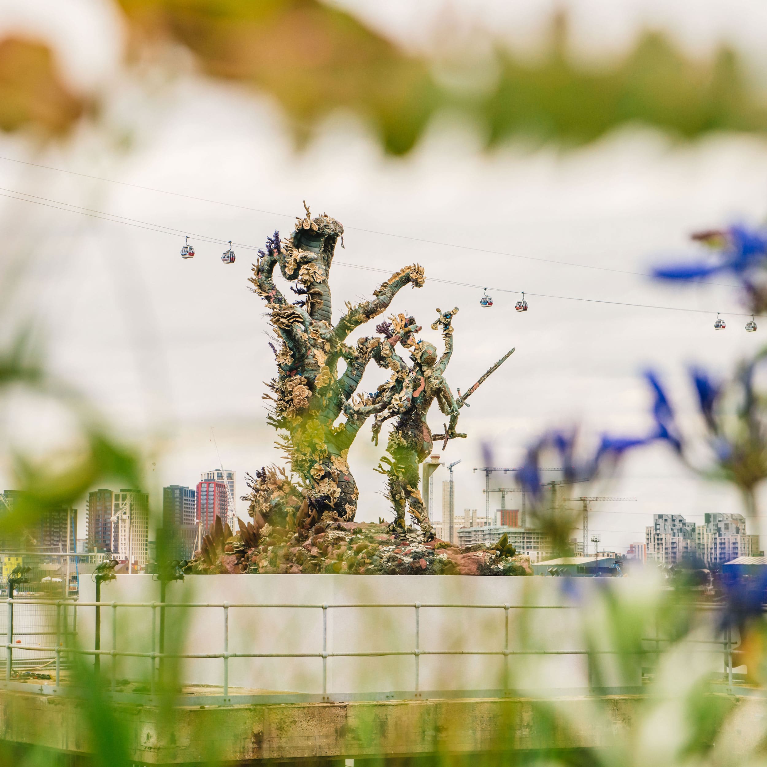 Closeup view of statues in the Greenwich Peninsula park with leaves and flowers surrounding the frame.