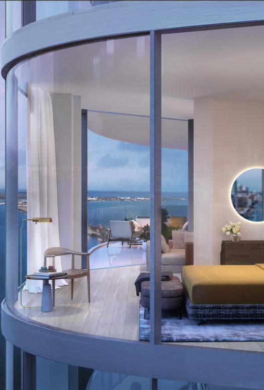 Exterior view of bedroom at Una Residences in Miami. A large bed, mirror & glass walls with attached bathroom and bay views.