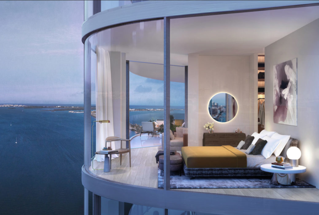 Exterior view of bedroom at Una Residences in Miami. A large bed, mirror & glass walls with attached bathroom and bay views.