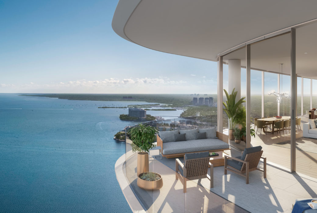 Exterior view of balcony overlooking the bay at Una Residences in Miami. Covered balcony with seating and potted plants.