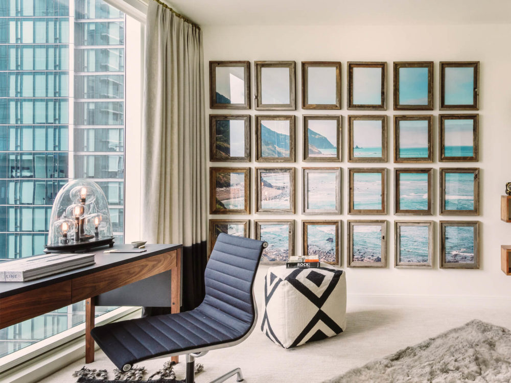 Living room at The Harrison condos in San Francisco. White wall with picture frames and a desk looking out oversized windows.