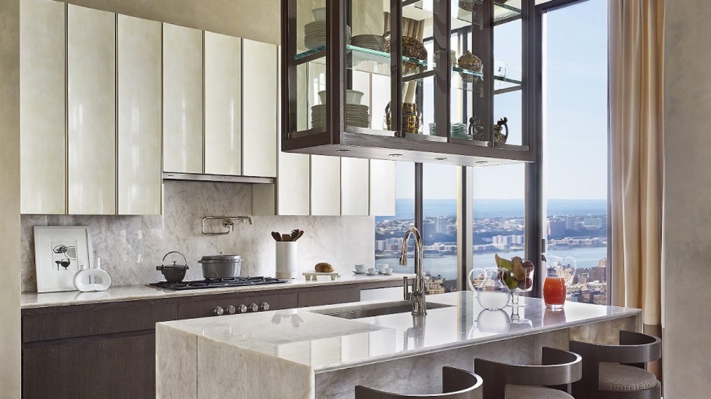 View of kitchen in 111 West 57th street condominiums with white table counters and black furniture with a window view of NYC.