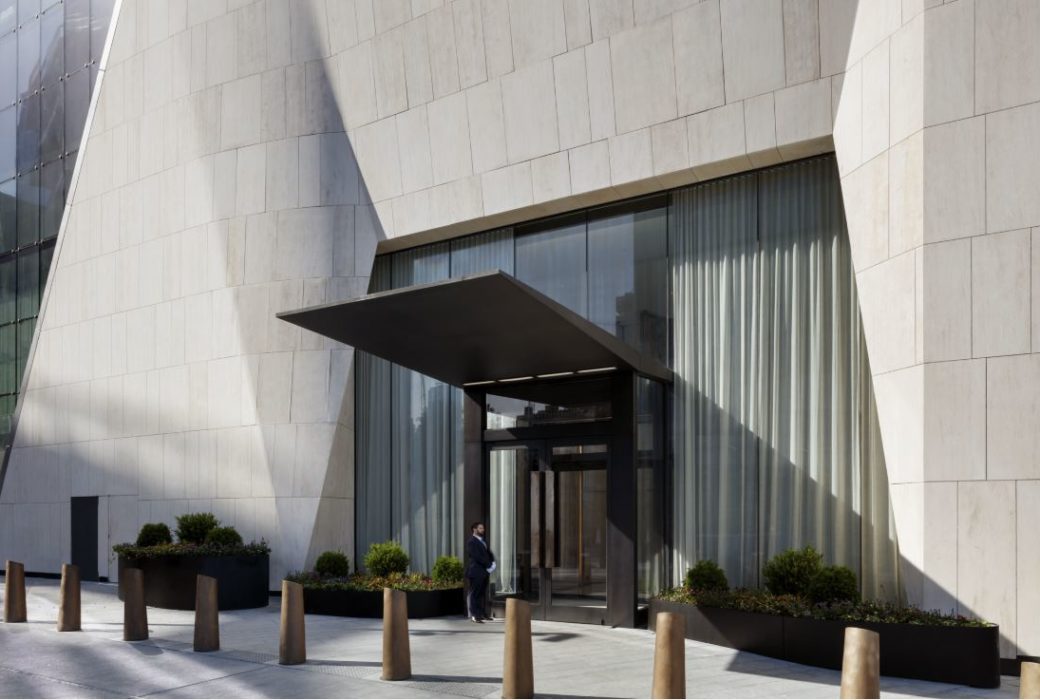 Exterior view on entrance to 15 Hudson Yards condominiums in New York City. White tile building with glass windows and doors.