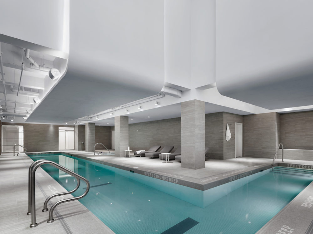 Interior view of 88 & 90 Lexington residence indoor pool in New York City. Has white walls, lounge chairs and long pool.