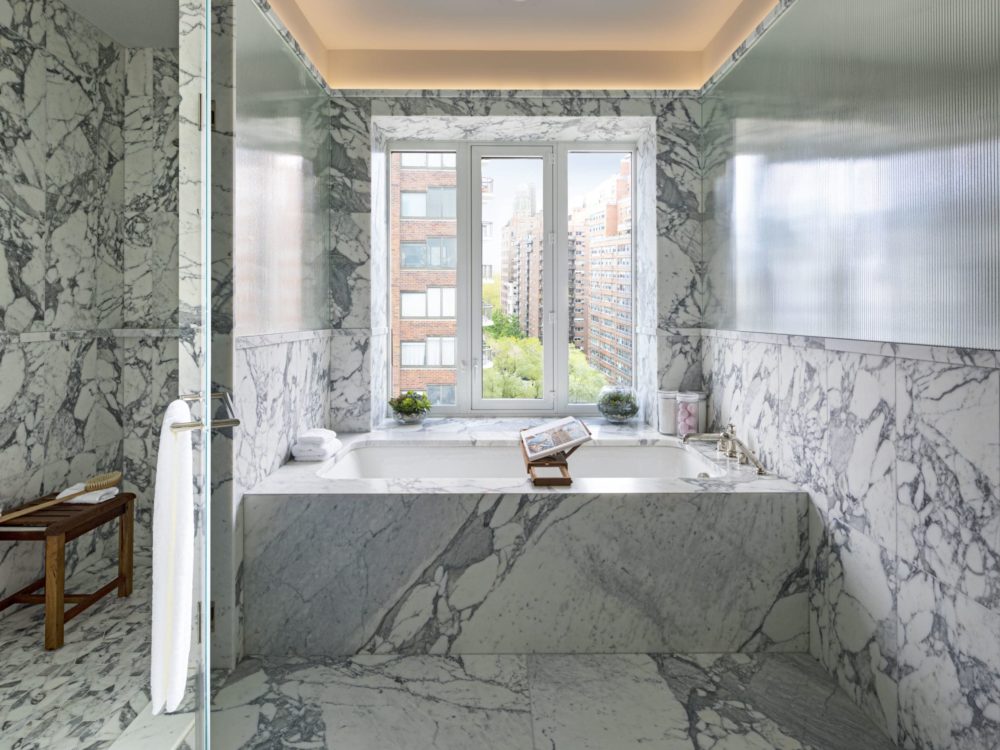 Interior view of 40 East End Ave residence master bathroom. Has marble walls and floors with bathtub and window view of NYC.