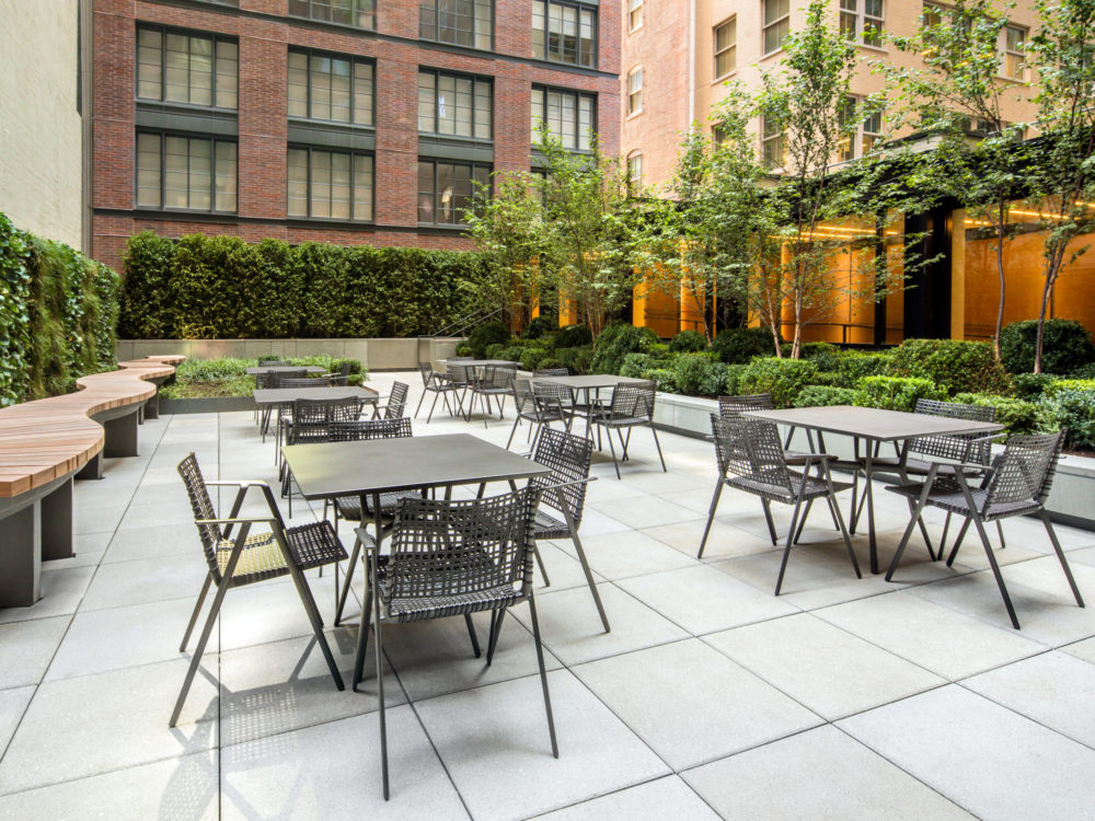 Exterior view of 70 Charlton condominiums outdoor lounge in New York City. Has dining tables, tile floors and green bushes.