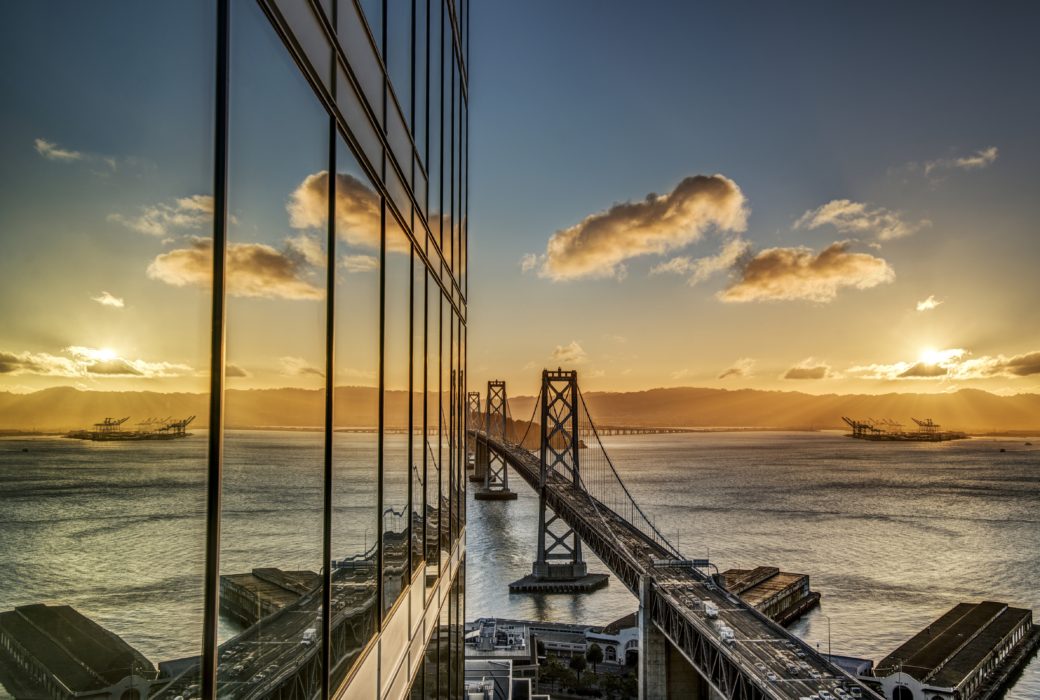 Exterior of The Harrison condos in San Francisco. Side of building with glass walls along the Bay Bridge during sunset.