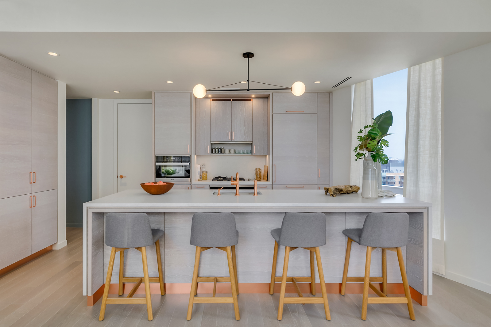 Interior view of Brooklyn Point residence kitchen with view of other buildings. Has white island countertop and wood floors.