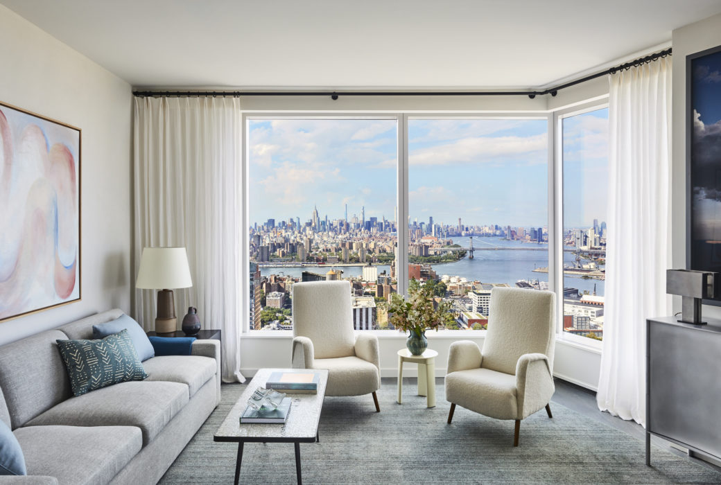 Interior view of Brooklyn Point residence living room with skyline window view. Has full furniture and white curtains.