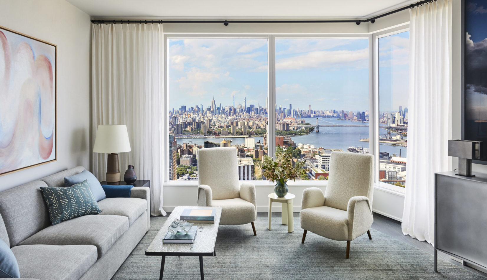 Interior view of Brooklyn Point residence living room with skyline window view. Has full furniture and white curtains.