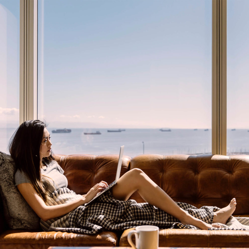 Living room view from The Harrison in San Francisco. Girl on a couch and oversized windows behind her with marina views..