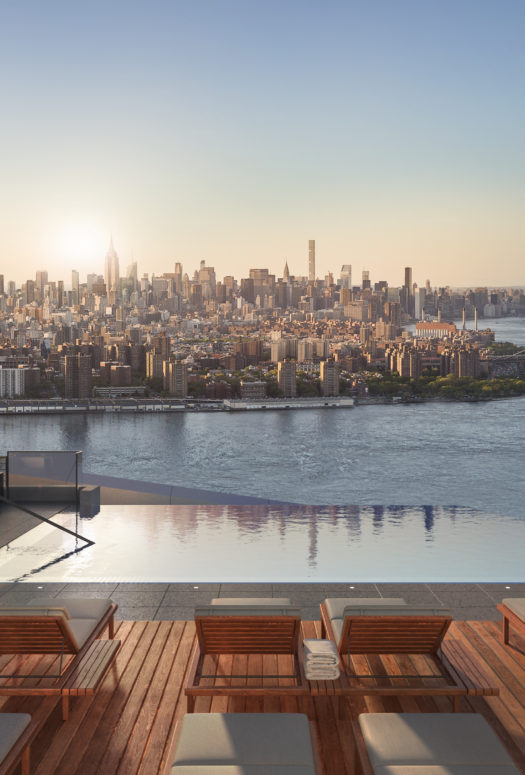 Exterior view of Brooklyn Point condominiums outdoor pool with river view and red lounging chairs in New York City.