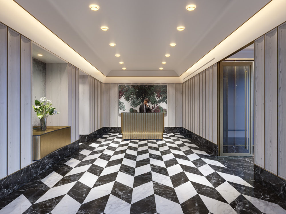 Interior view of lobby inside 40 East End Ave condominiums in NYC. Has checkered flooring, golden desk and white walls.