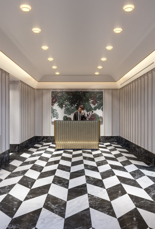 Interior view of lobby inside 40 East End Ave condominiums in NYC. Has checkered flooring, golden desk and white walls.