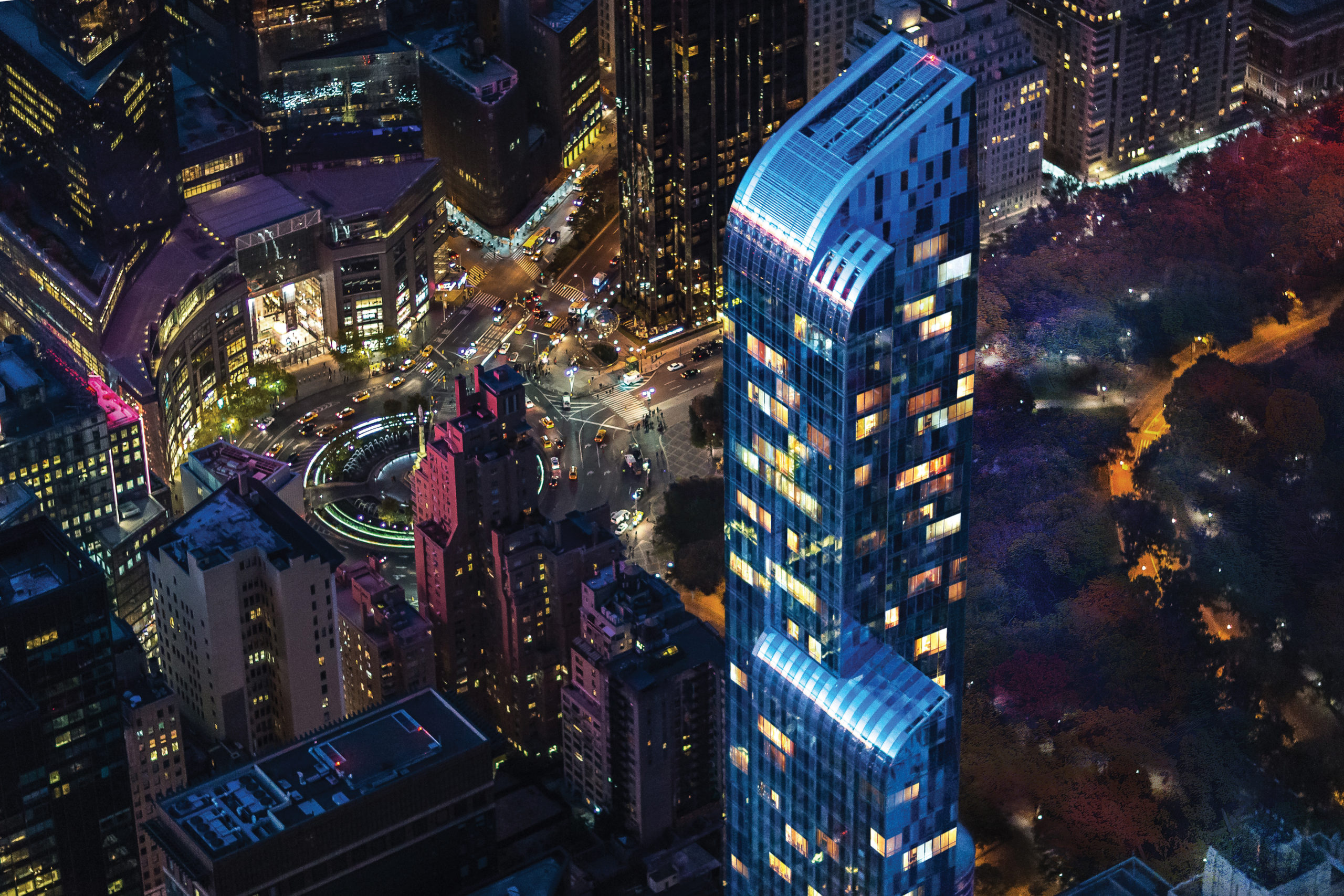 Night-time aerial view of One 57 luxury condominiums in New York City with lit up downtown background.