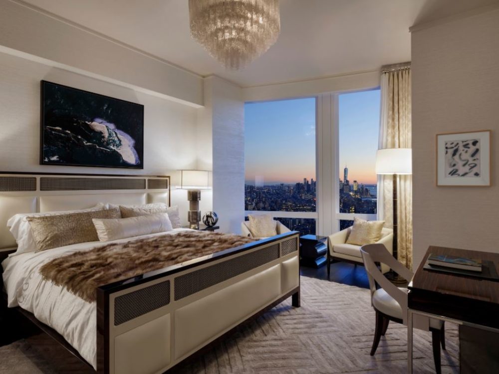 Interior view of 35 Hudson Yards residence master bedroom with window view of NYC. Has white walls, a bed, and a desk.
