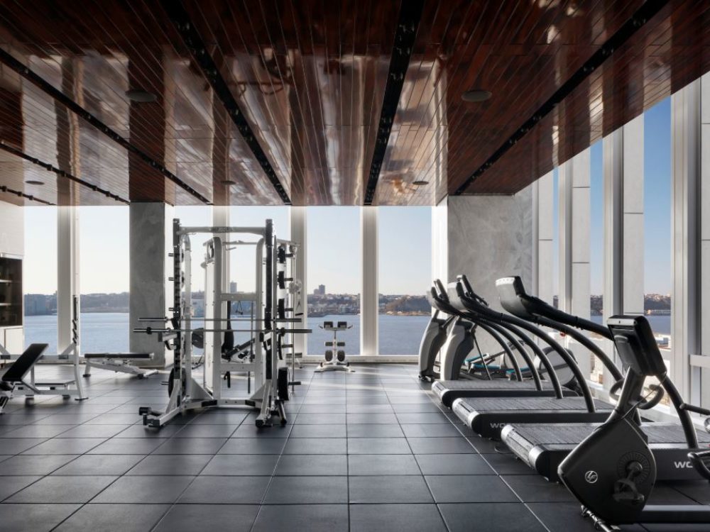 Interior view of 35 Hudson Yards residence fitness center with window view of NYC. Has cardio and weightlifting equipment.