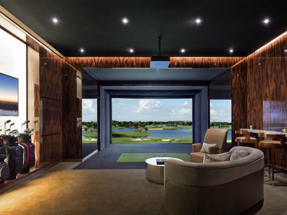 Interior view of 35 Hudson Yards residence golf lounge in NYC. Includes golf simulation, chairs, and a bar area.