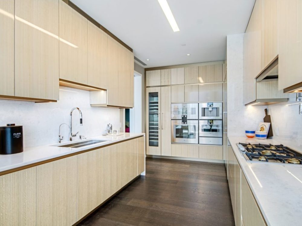 Interior view of 35 Hudson Yards residence kitchen in NYC. Includes wooden cabinets, wood floors, and white walls.