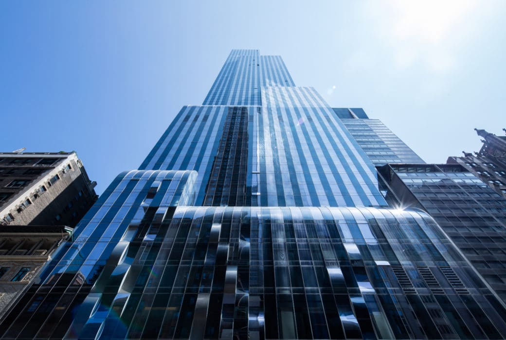 Street view of One 57 luxury condos in New York. Looking up at the residential tower with sun reflecting off the windows.