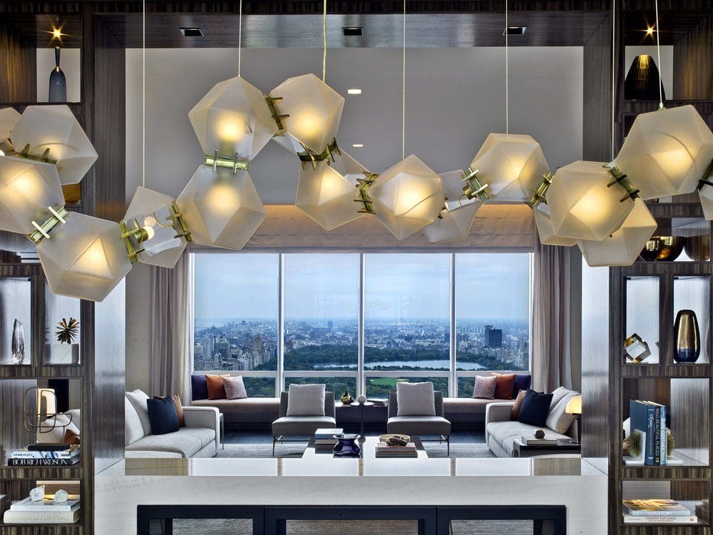 Living room with city views at One 57 condos in New York City. Hanging lights and bookshelves frame living room entrance.