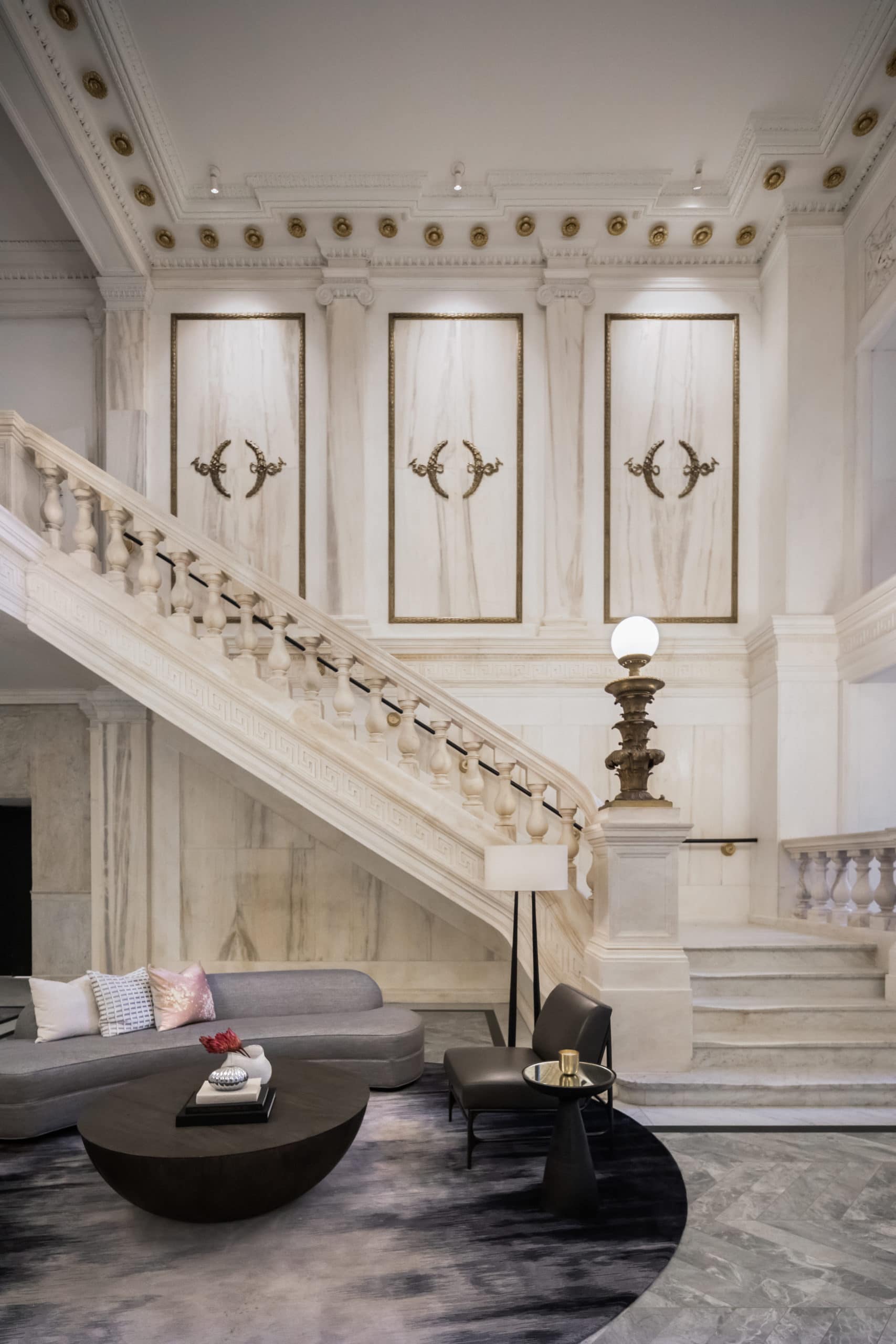 Interior view of a white, modern renaissance staircase and dark furniture part of the entrance of 108 Leonard in NYC.