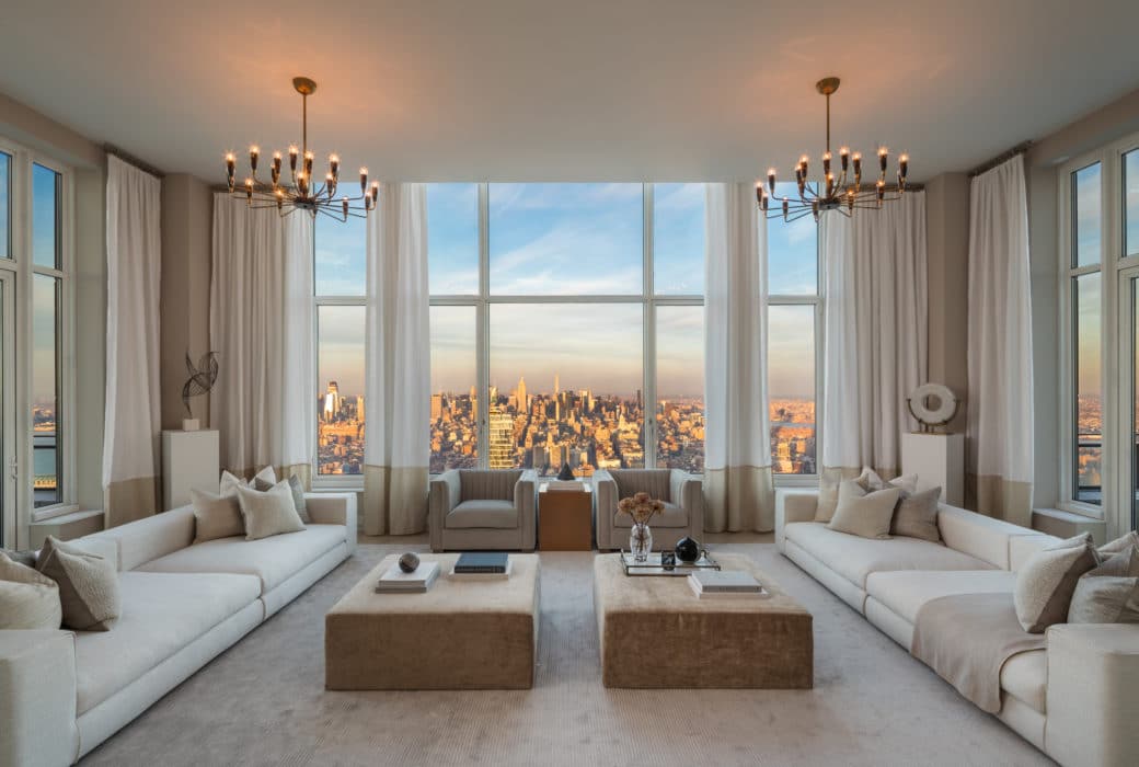 Interior view of living room inside 30 Park Place condominiums with window view of NYC. Has white walls and wood tables.