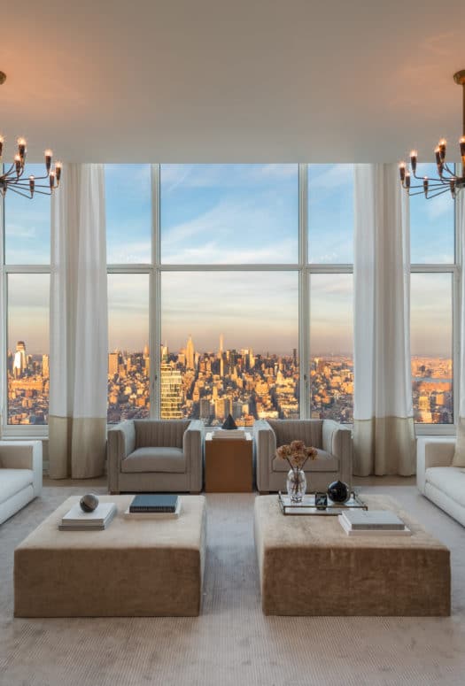 Interior view of living room inside 30 Park Place condominiums with window view of NYC. Has white walls and wood tables.