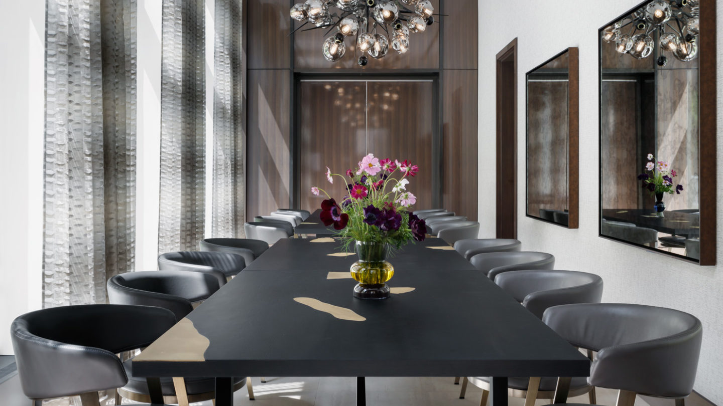 Private dining room at the Park Loggia luxury condos in New York. Long black dining table, tall windows, & large chandelier.
