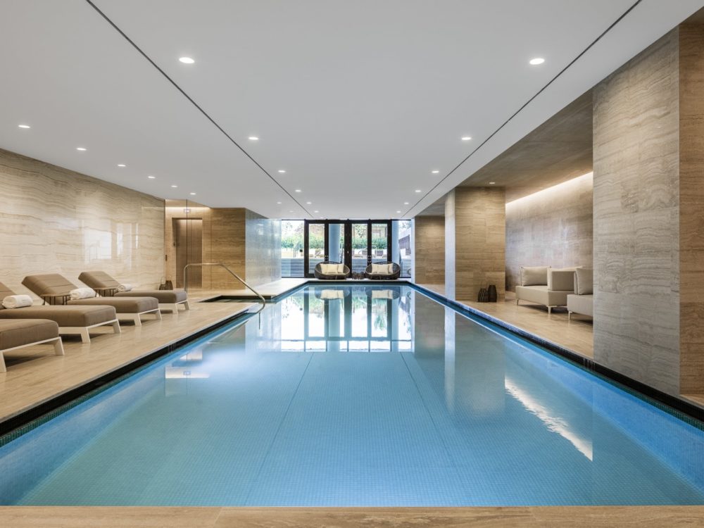 Interior view of Arte Surfside condominiums indoor pool with lounge chairs, framed door windows and rectangular pool.