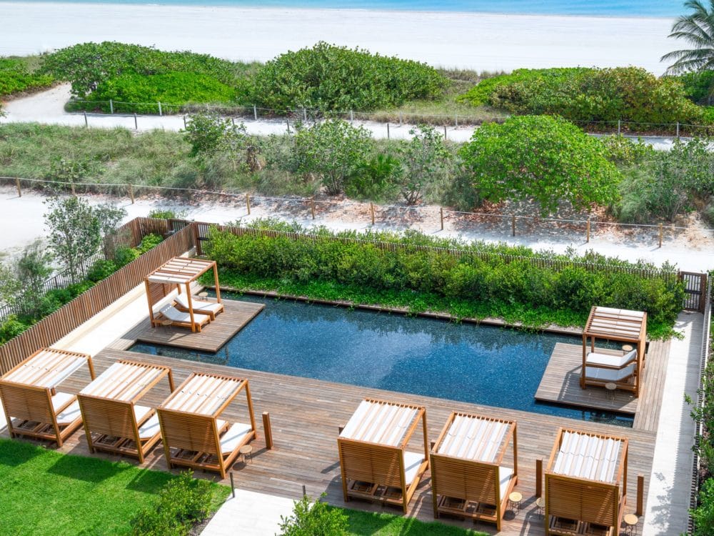 Exterior view of Arte Surfside condominiums oceanfront pool area. Has wooden platform and cabana chairs.