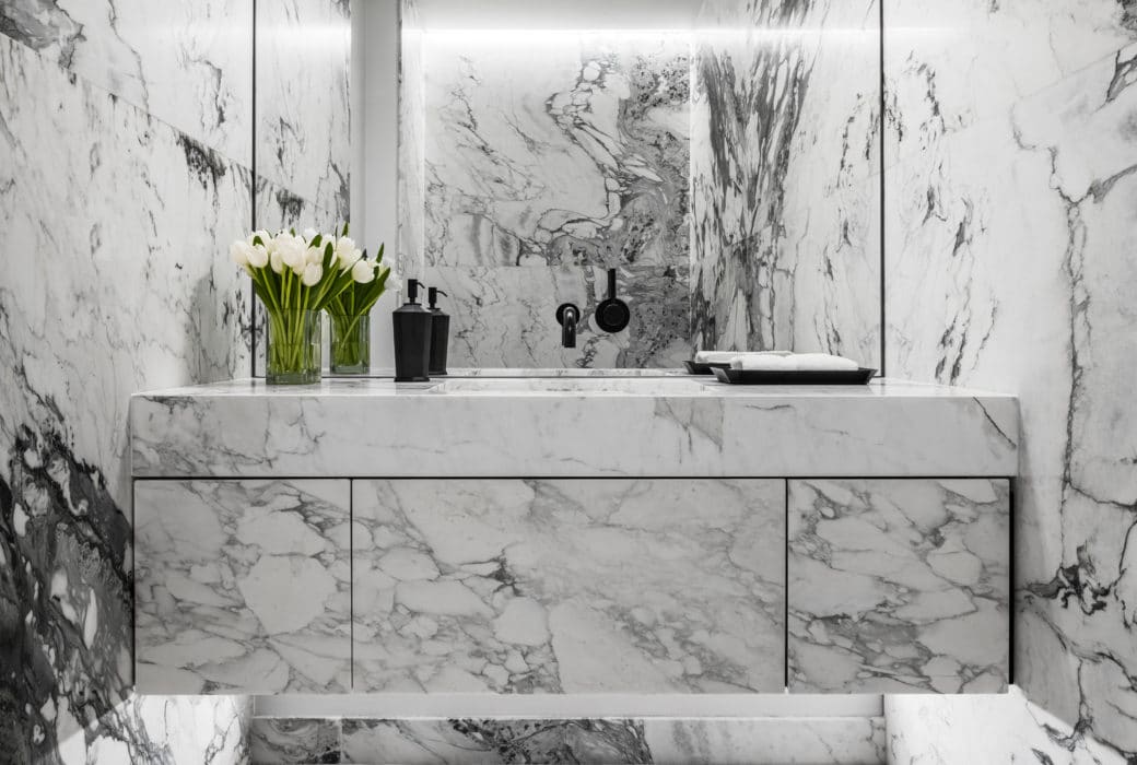 Bathroom at Monad Terrace condominiums in Miami. Veined stone make up the floor, walls, and vanity with full mirror and sink.