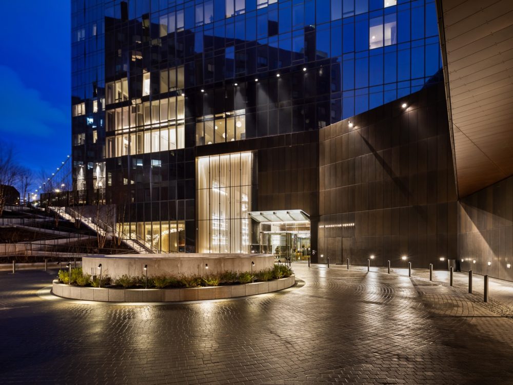 Exterior of One Manhattan Square condos in New York. Driveway with round about and well lit carport at entrance to building.