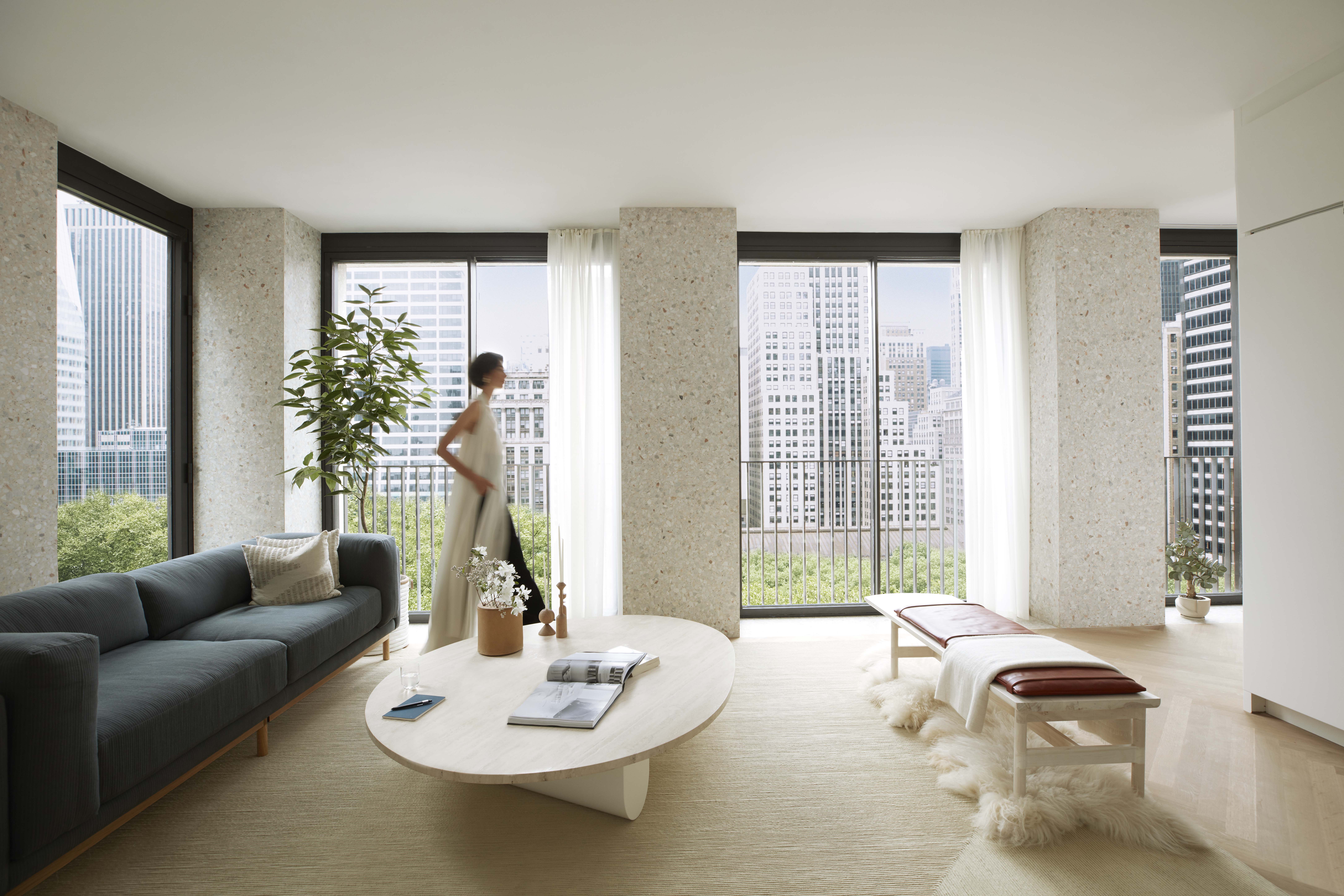 Living room at The Bryant condos in New York. Woman walking in front of the oversized windows overlooking Bryant Park.