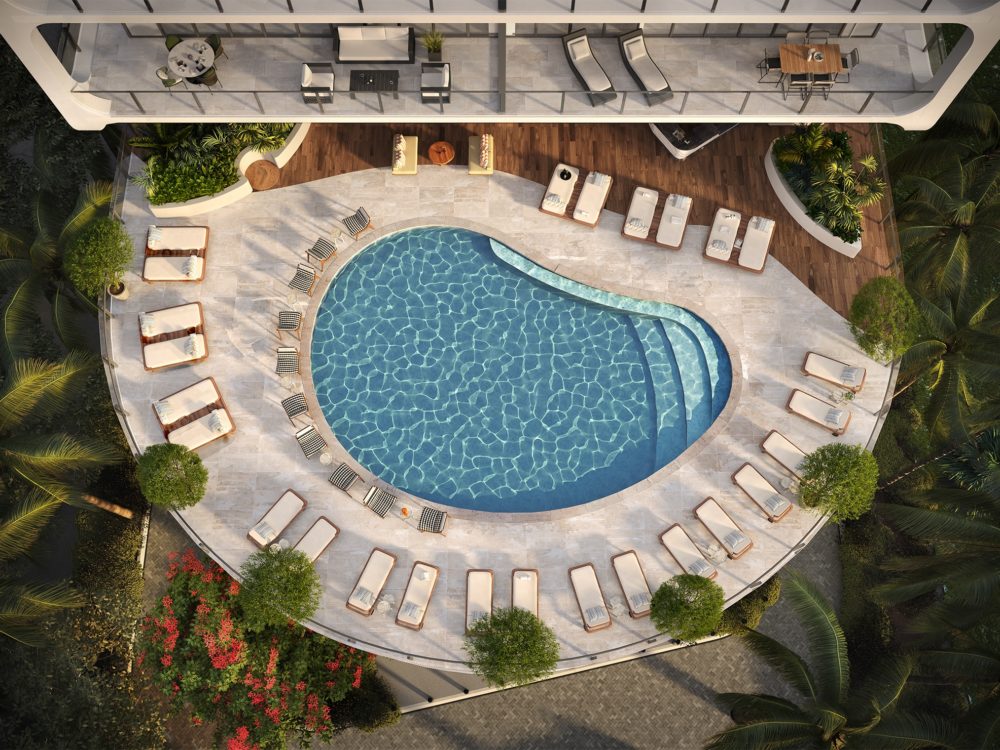 Aerial view of outdoor pool at Mr. C Residences in Miami. Pool at condo complex bordered by lounge chairs and trees.