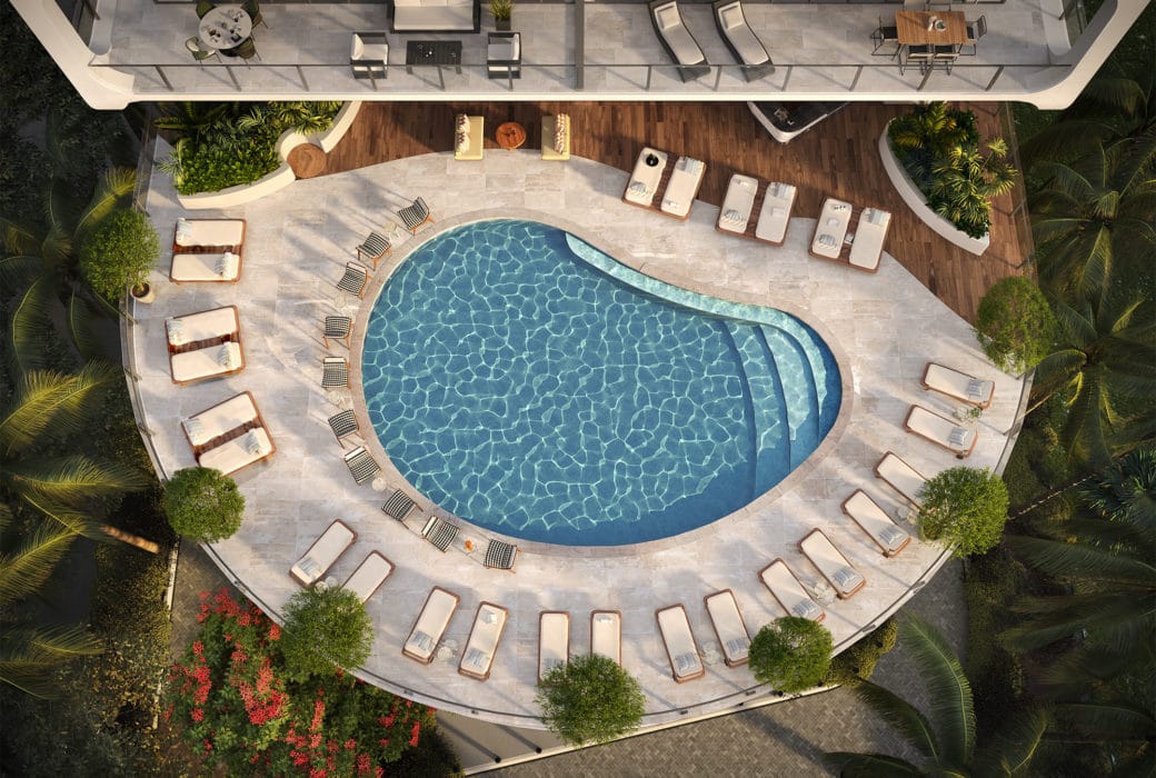 Aerial view of outdoor pool at Mr. C Residences in Miami. Pool at condo complex bordered by lounge chairs and trees.
