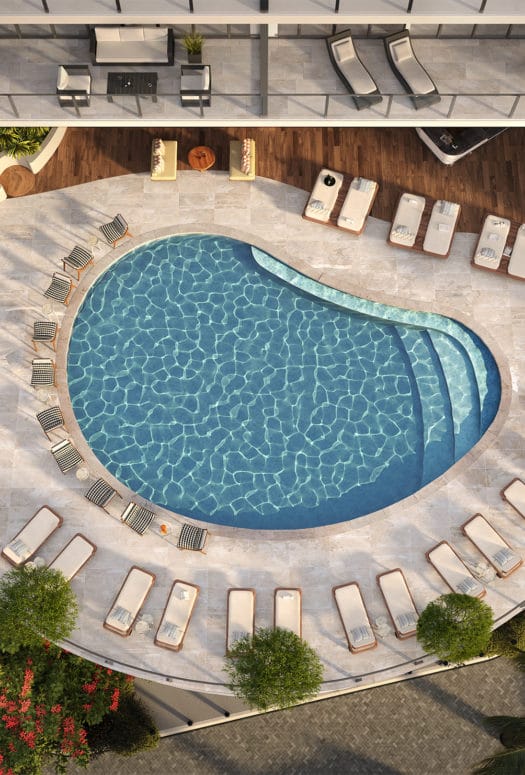 Aerial view of outdoor pool at Mr. C Residences in Miami. Pool at condo complex bordered by lounge chairs and trees.