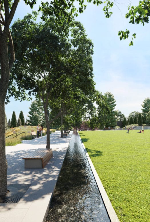 Lawn and park between the tower of Waterline Square in New York. Cement walkway with trees and benches border the lawn.