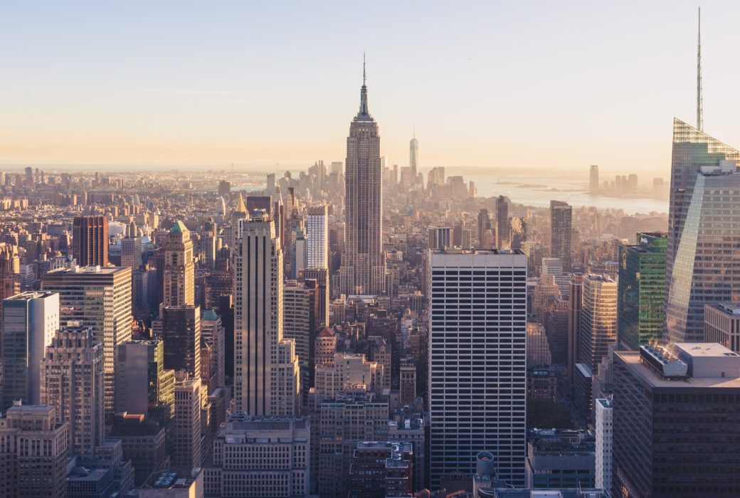 Daytime picture of the New York City skyline. Light haze in the background of downtown buildings and skyscrapers.