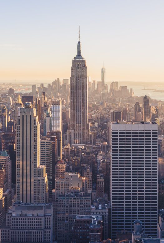 Daytime picture of the New York City skyline. Light haze in the background of downtown buildings and skyscrapers.