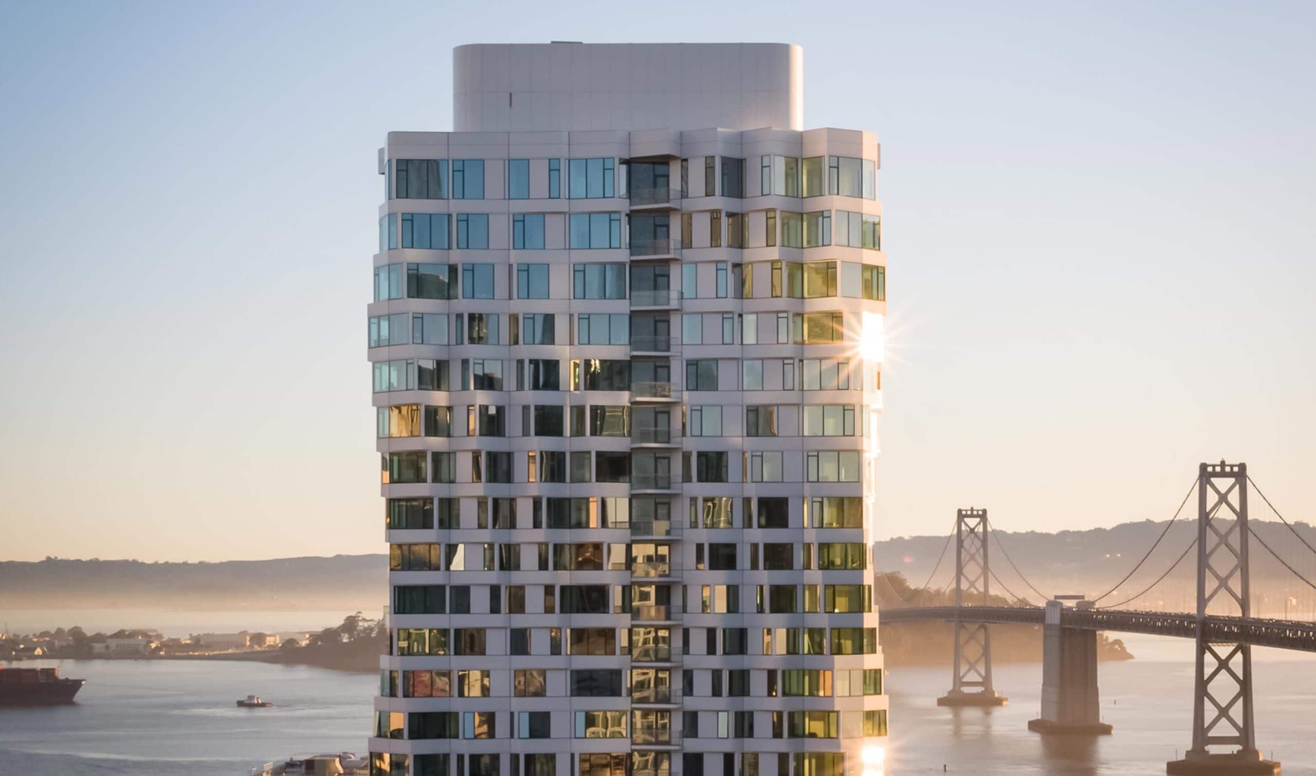 Superman view of Mira Tower luxury residences in San Francisco. Spiral tower with Bay Bridge in the background at sunrise.