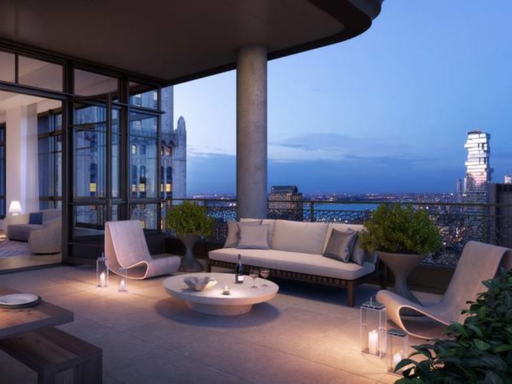 Exterior view of vignette dining area inside 25 Park Row condominiums with skyline view of New York City during the night.