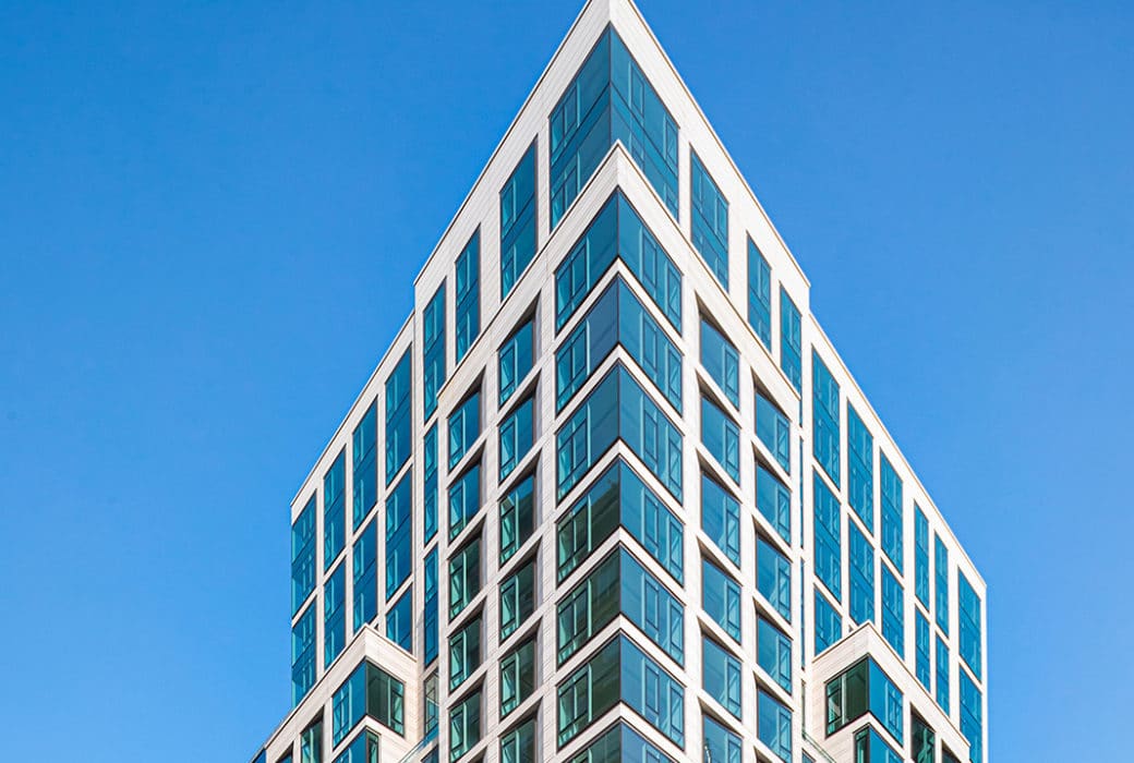 Exterior view of The Hayworth condominium in New York. Top floors of high rise building with large windows and white framing.