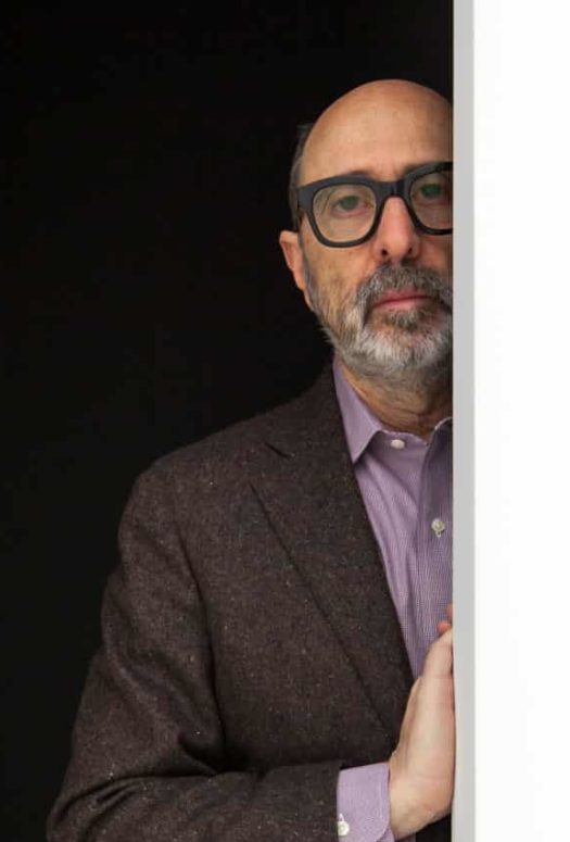 Architect Isay Weinfield. Man with glasses standing half hidden in a doorway with his right hand resting on a white wall.