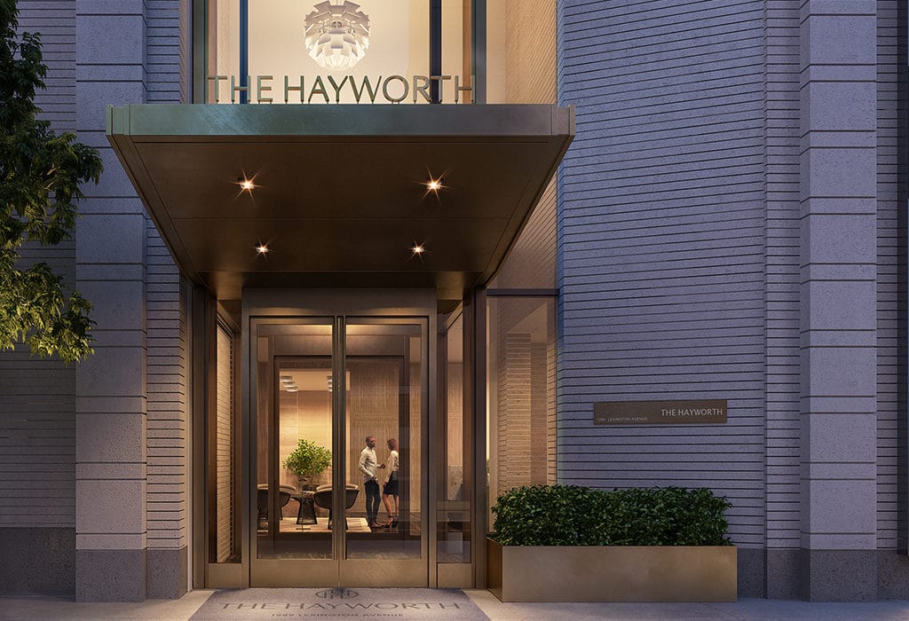 The Hayworth Condos entrance in New York City. Bronze double doors, potted bushes, and a well lit canopy cover.